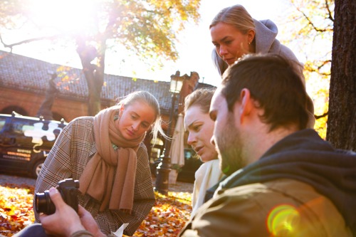 Fire studenter på digital innholdsproduksjon er samlet rundt et kamera, som de alle ser på. 