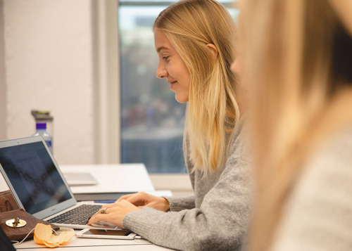 Bilde av ung kvinne med blondt hår som sitter foran en laptop.