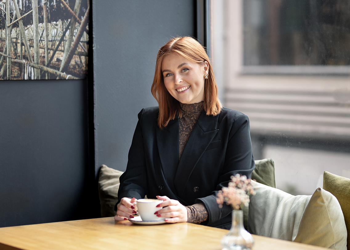 Ida-Marie sitter ved et bord på et kontor, med en kaffekopp i hendene.