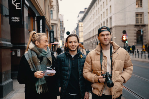 Foto av en kvinnelig og to mannlige studenter ute på gaten, med notatblokk og kamera.