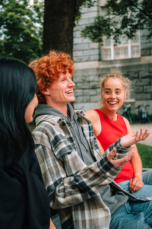 Tre studenter sitter på en benk i en park og snakker sammen.