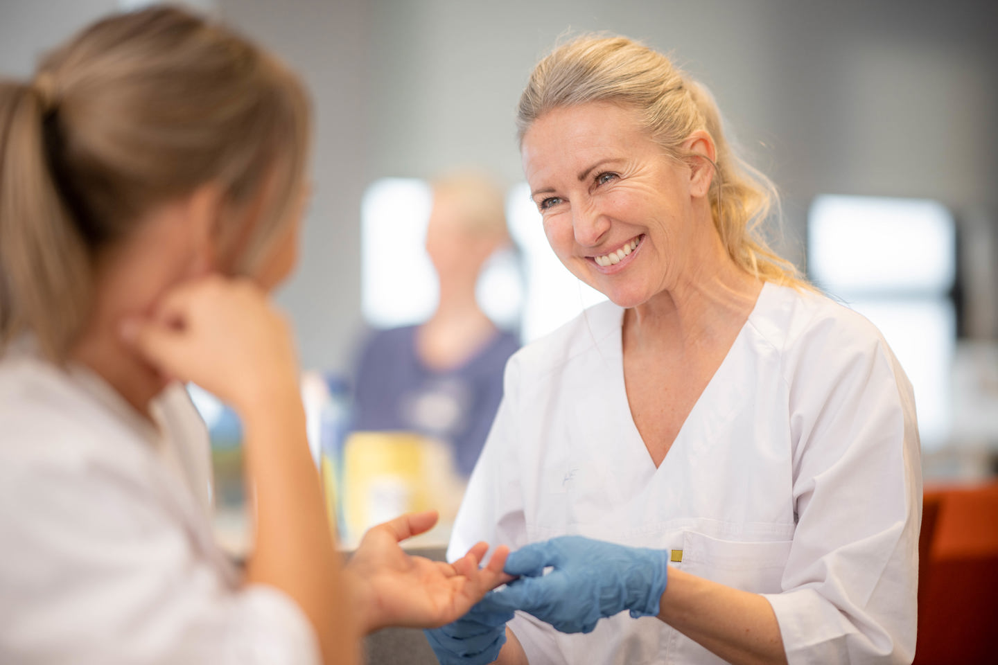 Helsearbeider i hvit arbeidsuniform bruker blå hansker mens hun utfører en praktisk prosedyre på en annen person