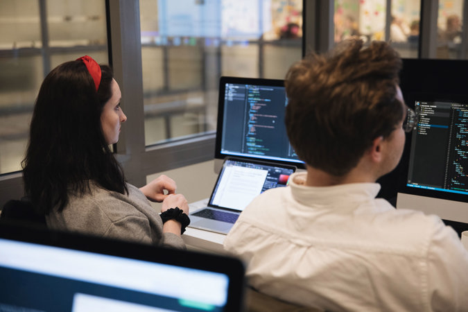 To studenter jobber med frontend-utvikling på datamaskinene sine i klasserommet.