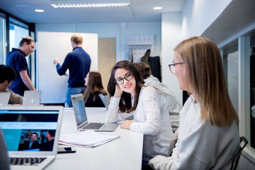 Foto av kvinnelige studenter i et grupperom med hver sin laptop.