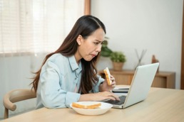 Kvinne som spiser brød mens hun sitter foran pc-skjermen.