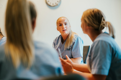 Tre kvinnelige osteopatistudenter ved Kristiania er fotografert sittende ved et bord mens de livlig diskuterer