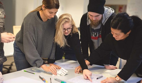 Tre reklamestudenter på Fagskolen Kristiania har en idémyldring i klasserommet sammen med fagansvarlig Aranya Pascale Rusli. 