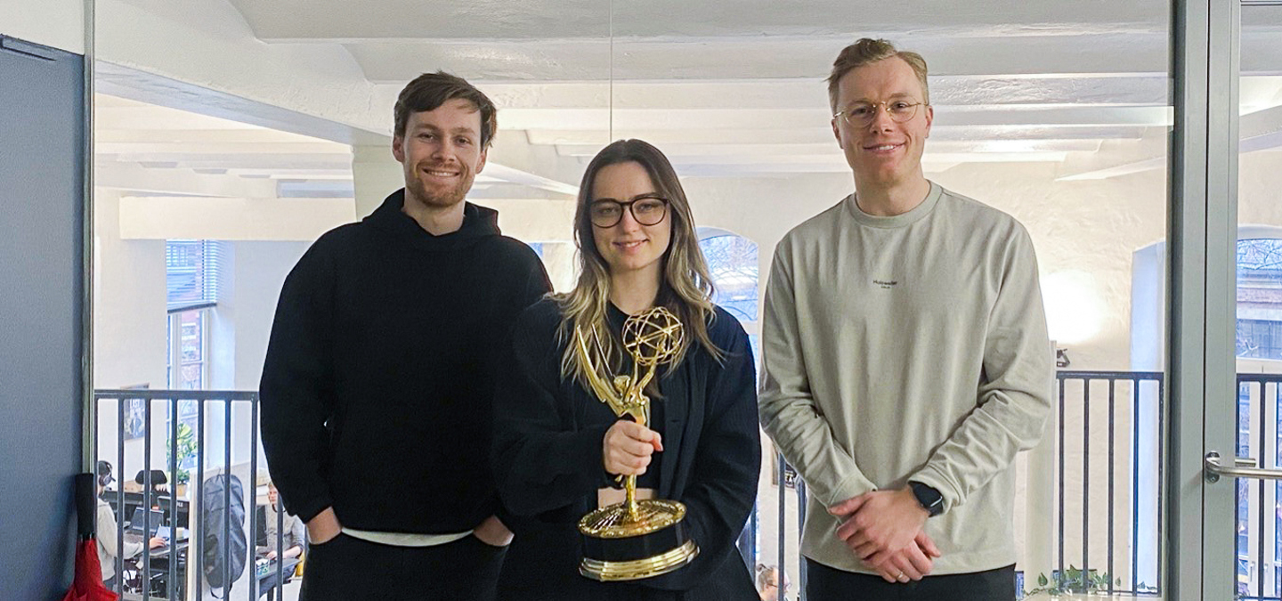 Melvin, Ingvild og Markus poserer i et kontorlandskap med en Emmy-statuett.