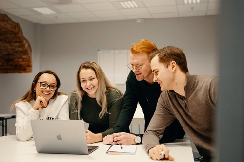 Studenter flokker rundt en laptop i et studierom.