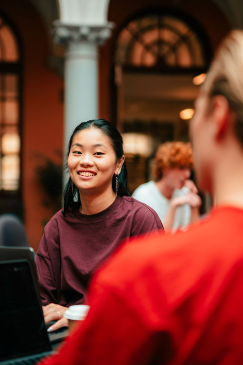 Tre studenter sitter i et atrium, bak dem ser man en klassisk romersk søyle.