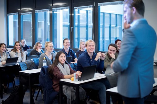 Foto av studenter som sitter i klasserommet og blir undervist av foreleser. 