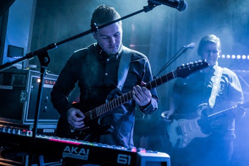 Foto av mannlig gitarist som spiller på en mørk scene. 