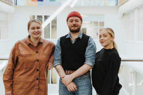 Tre studenter står ved et rekkverk i et atrium.