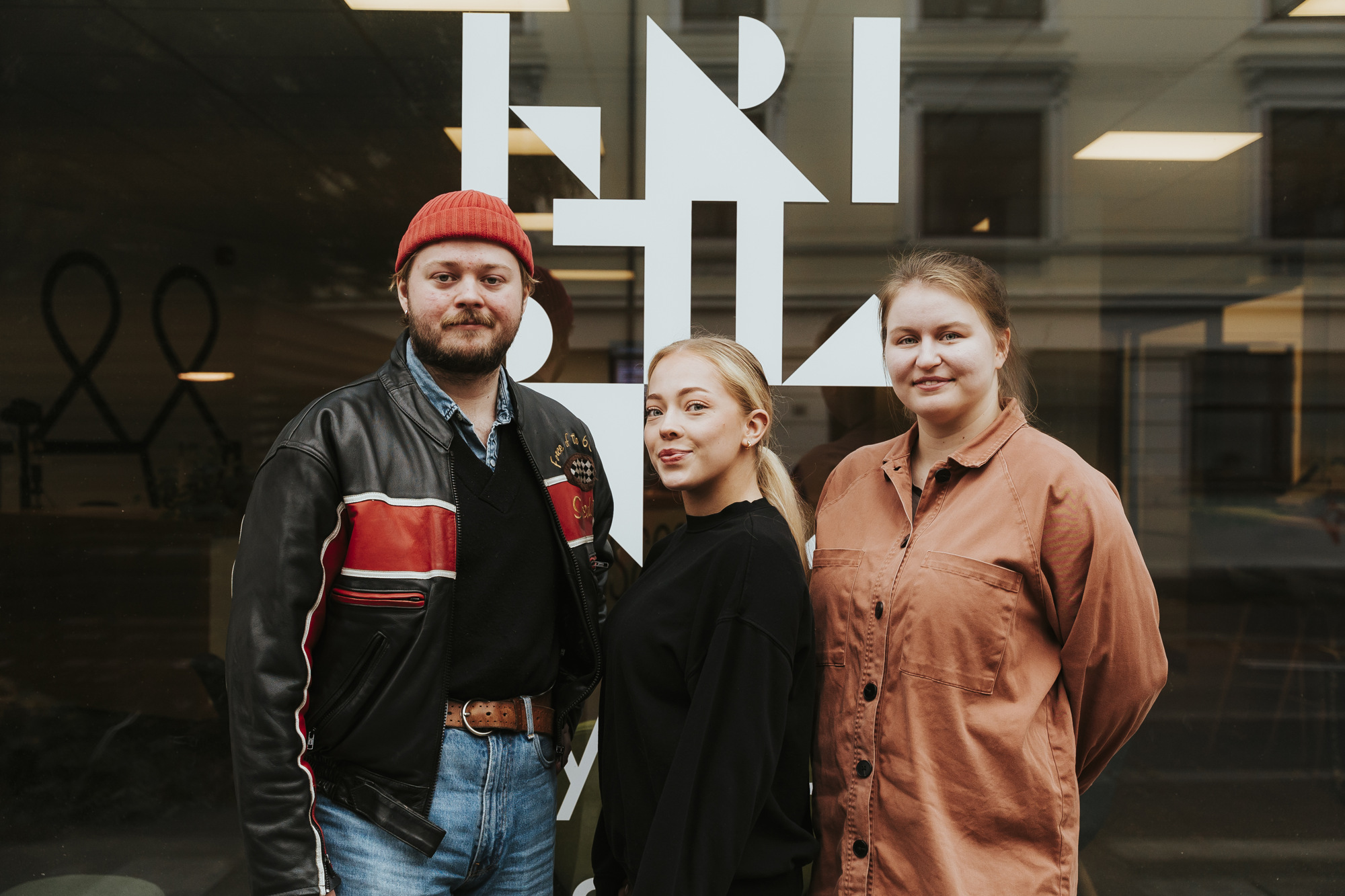 Tre studenter står foran en Kristiania-logo på en glassvegg.