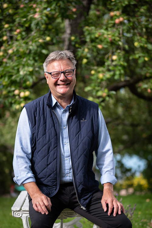 Foto av Trond Adland i et parklandskap, mens han lener seg mot et bord.