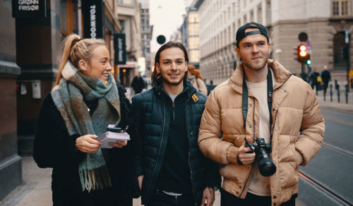 Foto av studenter som vandrer langs en gate med notatblokk og kamera.