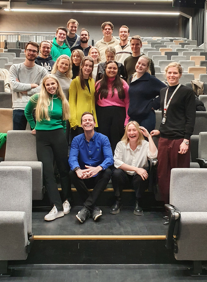 19 studenter i tjenestedesign oppstilt i midtgangen i en forelesningssal.