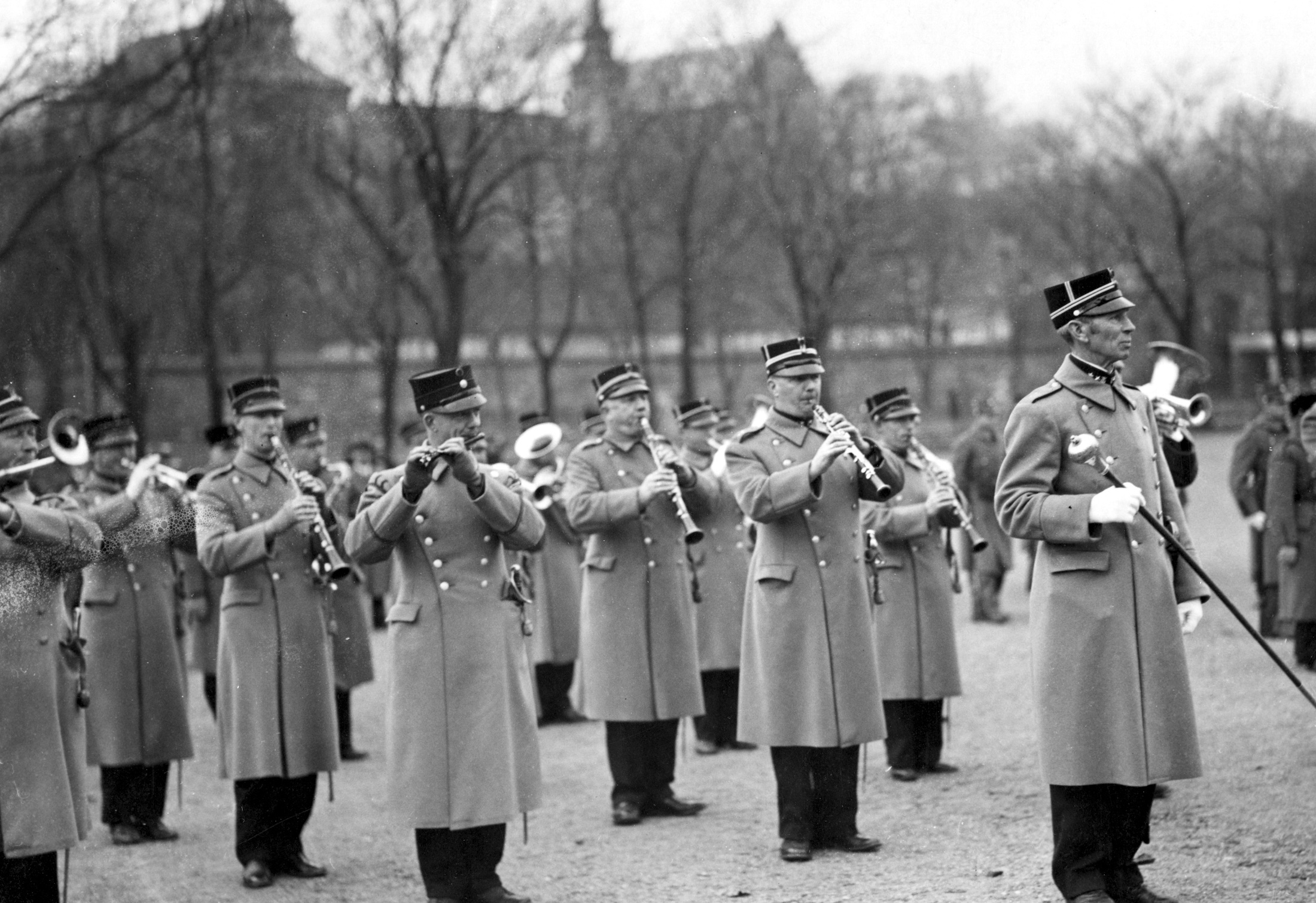Vi ser en leder og korpset bak i eldre uniformer, som spiller på ulike instrumenter.