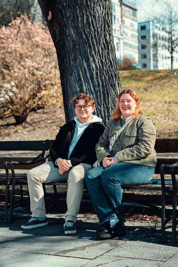 Snorre og Maria sitter på en benk foran ett tre.