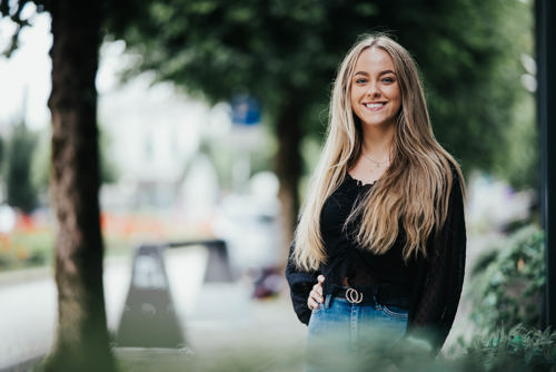 Portrett av Anniken, som står i en gate med trær langs siden.