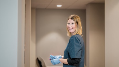 Helsepersonell med engangshansker står i en korridor og smiler inn i kamera