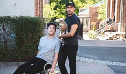 Foto av to unge menn i en gate. En mann holder en katt.