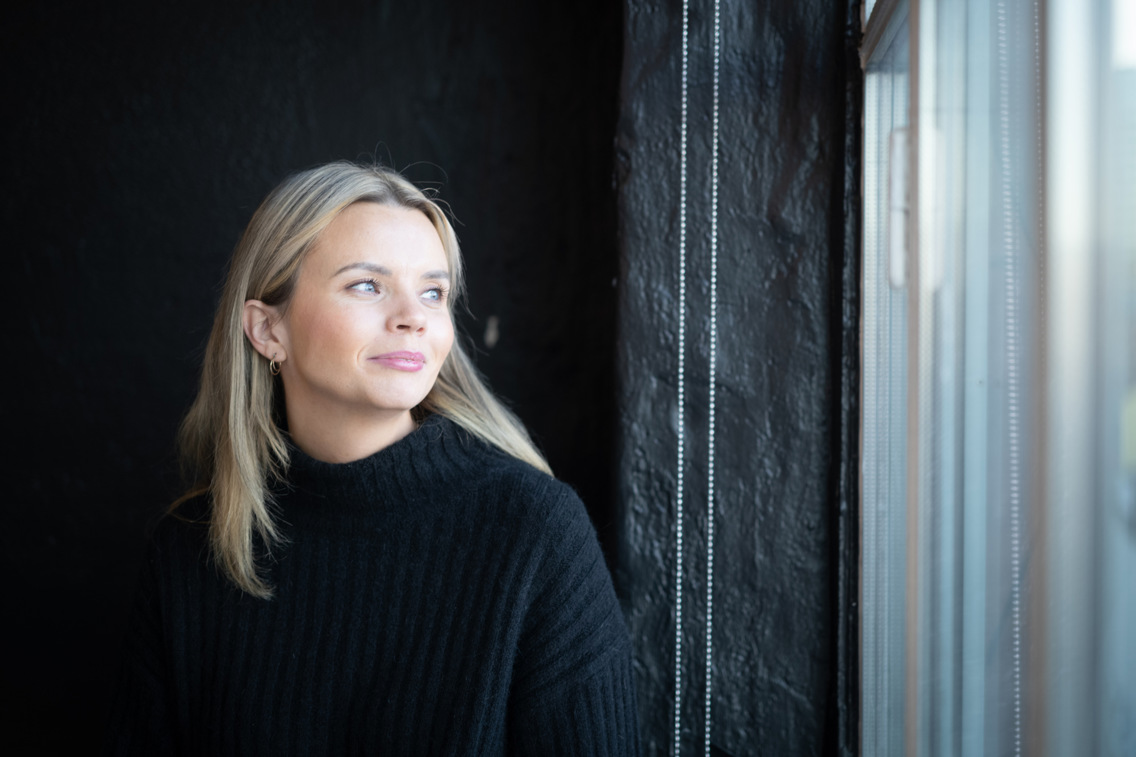 Portrett av Sofie står i mørkt rom og ser ut av vinduet.