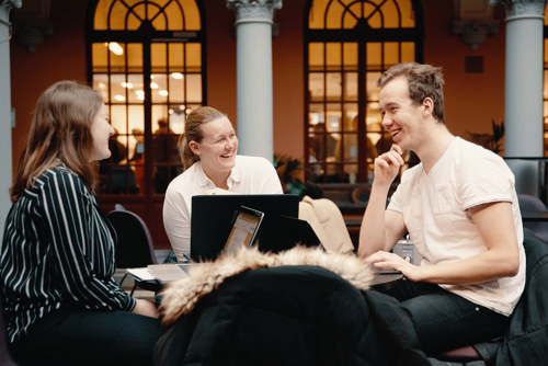 Foto av to kvinnelige og en mannlig student rundt et bord som snakker sammen.