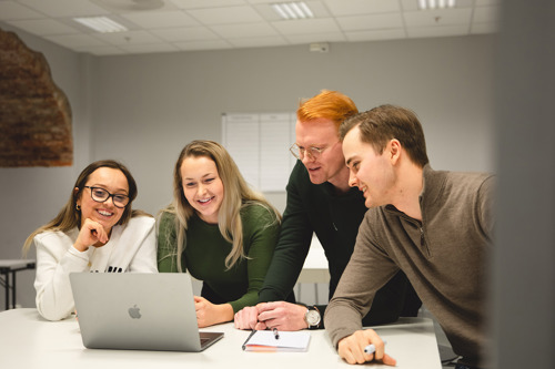 Foto av to kvinnelige og to mannlige studenter som er samlet rundt en laptop på et grupperom.