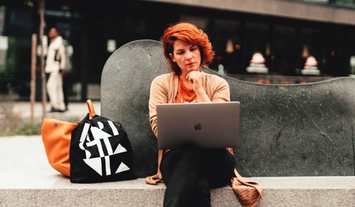 Student som sitter på en benk med en Mac på fanget