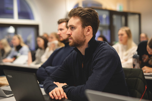 Ung mann som sitter i et klasserom på Høyskolen Kristiania