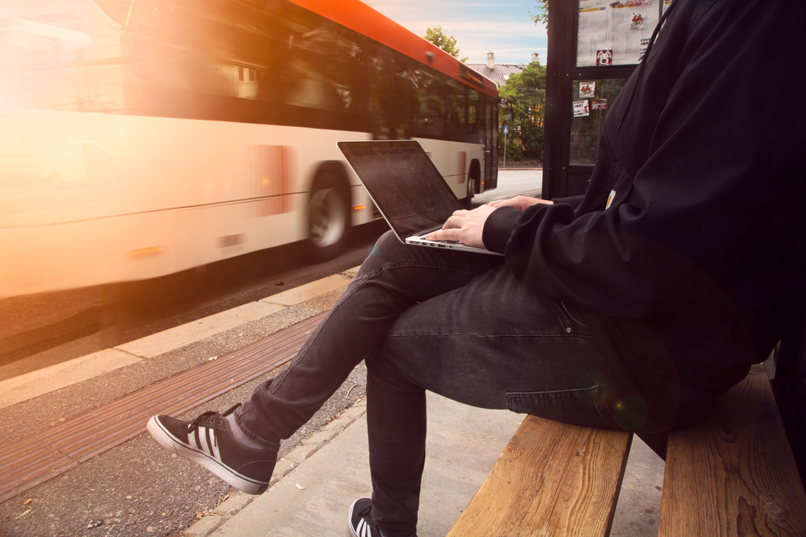 Foto av en person ved et busstopp med en laptop.