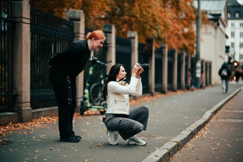 To studenter står på en gate. En av kvinnene tar et bilde, mens den andre kvinner står i bakgrunnen og ser på