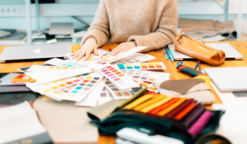 En student ser på fargeprøver. På pulten er det penal, tegnesaker og tekstilprøver.