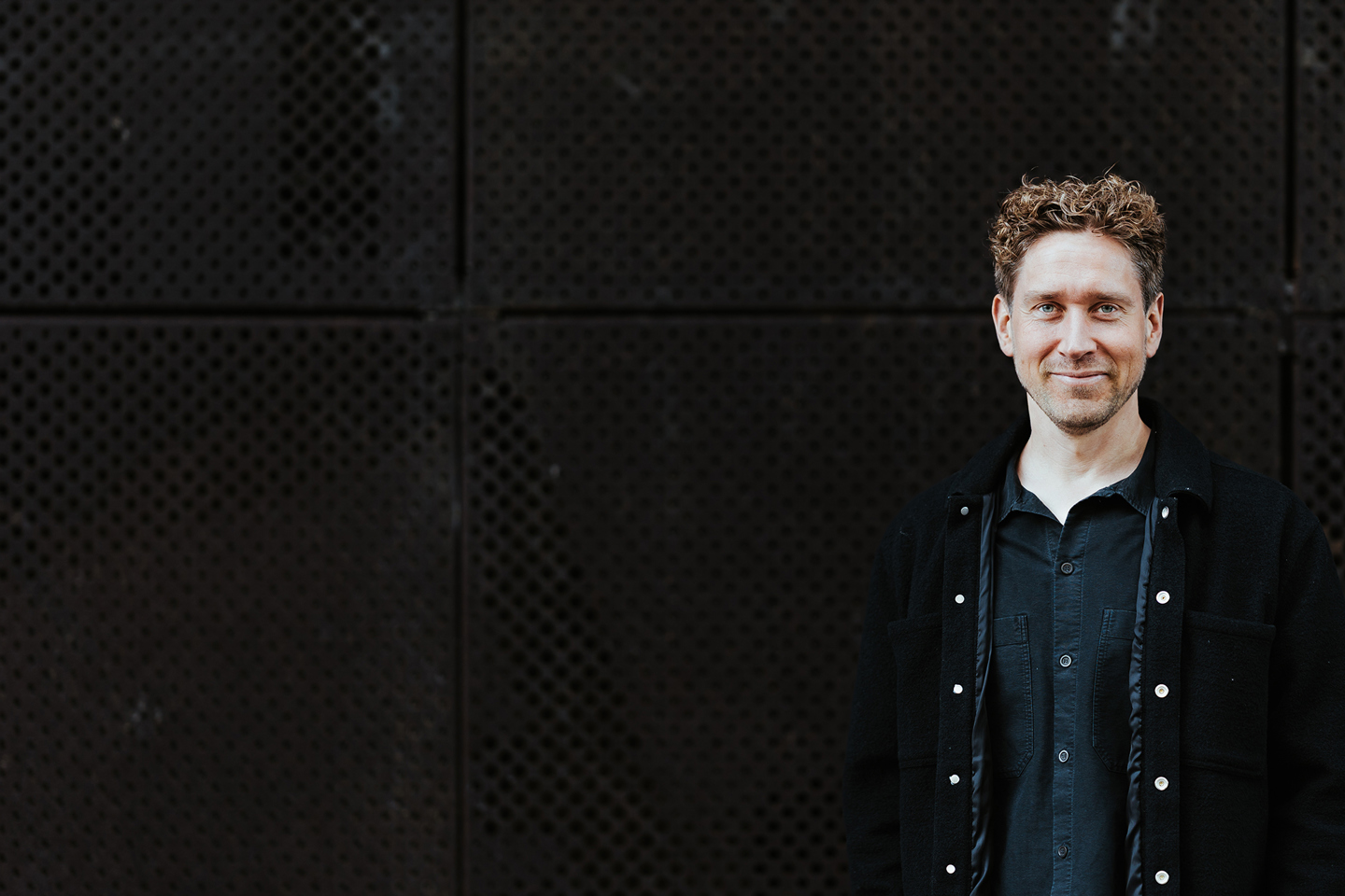 Portrettbilde av en mann med industriell bakgrunn. Mannen smiler og ser blid ut.